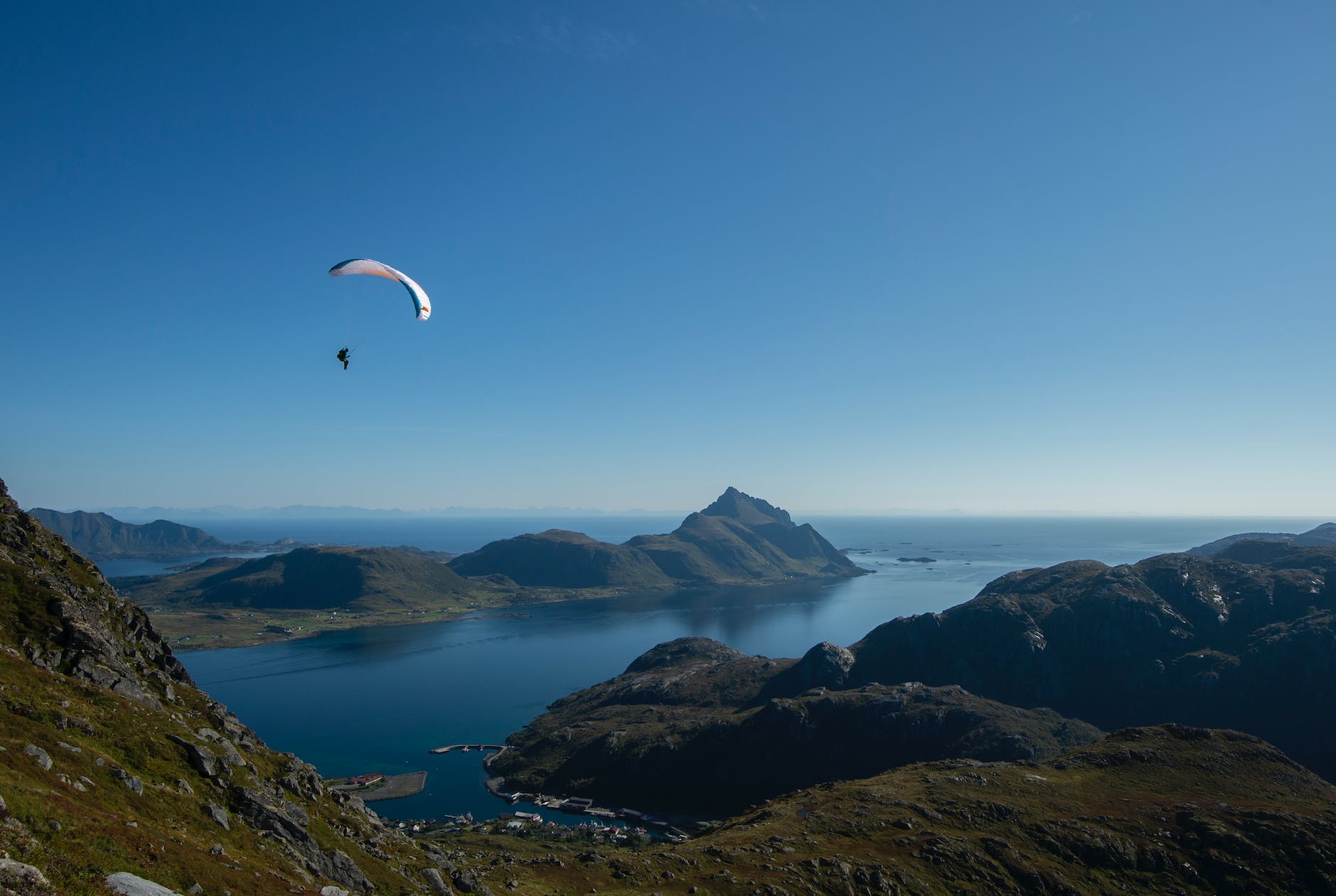 unrecognizable tourist on paraglider flying above ocean and mountains
